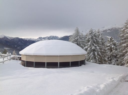Auch bei Schnee kein Problem Runde, schneebedeckte Struktur umgeben von verschneiten Bäumen in winterlicher Landschaft.