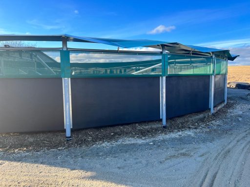 Windschutznetze Ein runder unterteilte Behälter mit grünem Netz und blauer Umrandung, umgeben von sandigem Boden.