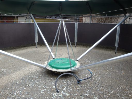 Montage ohne Fundament Kreisförmige Plattform mit grüner Oberfläche, umgeben von metallenen Stützen und Bodenbelag.